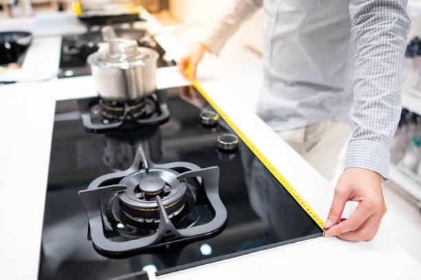 Male hand interior designer using tape measure on gas stove on modern countertop in kitchen showroom. Shopping appliance for domestic kitchen. Home improvement concept