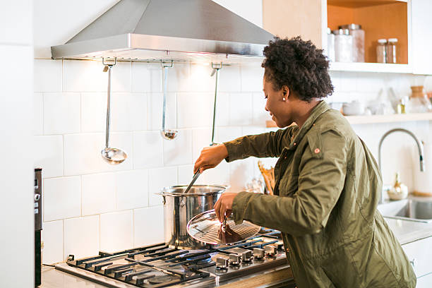 Woman cooking meal with chimney hood extracting smoke.