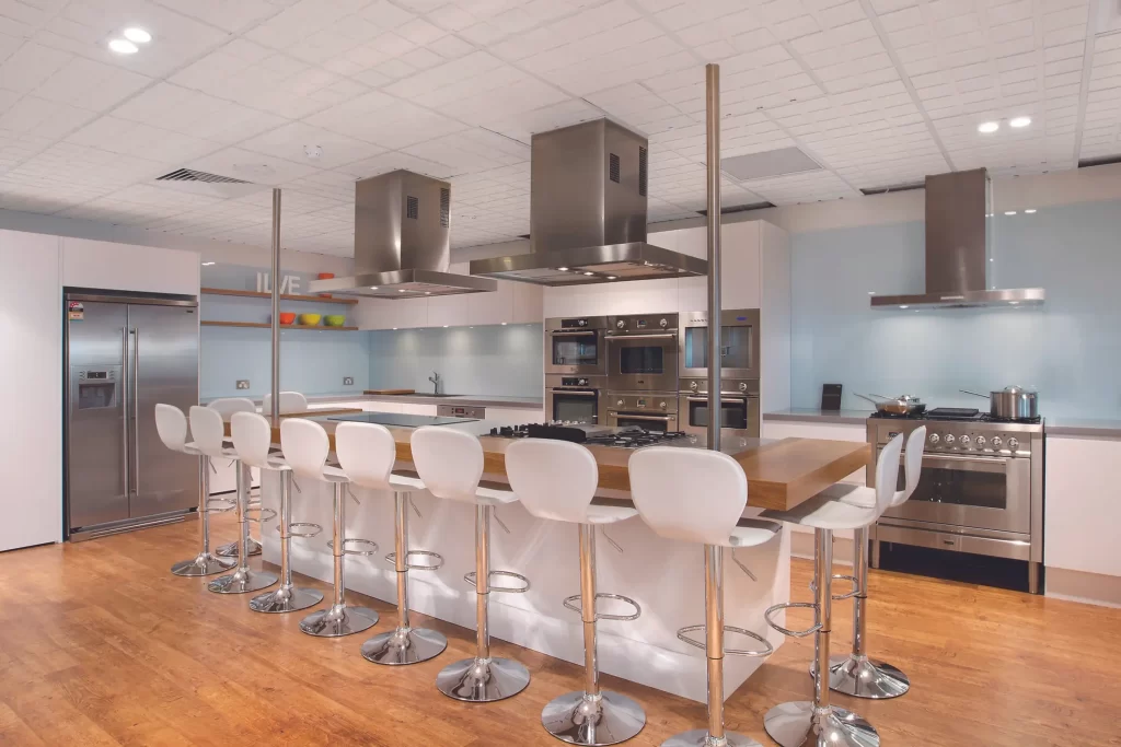 A Kitchen Design with Two Island Kitchen Hoods, A Wall Hood, Inbuilt Induction and Stainless Steel Cooker, and Fridge